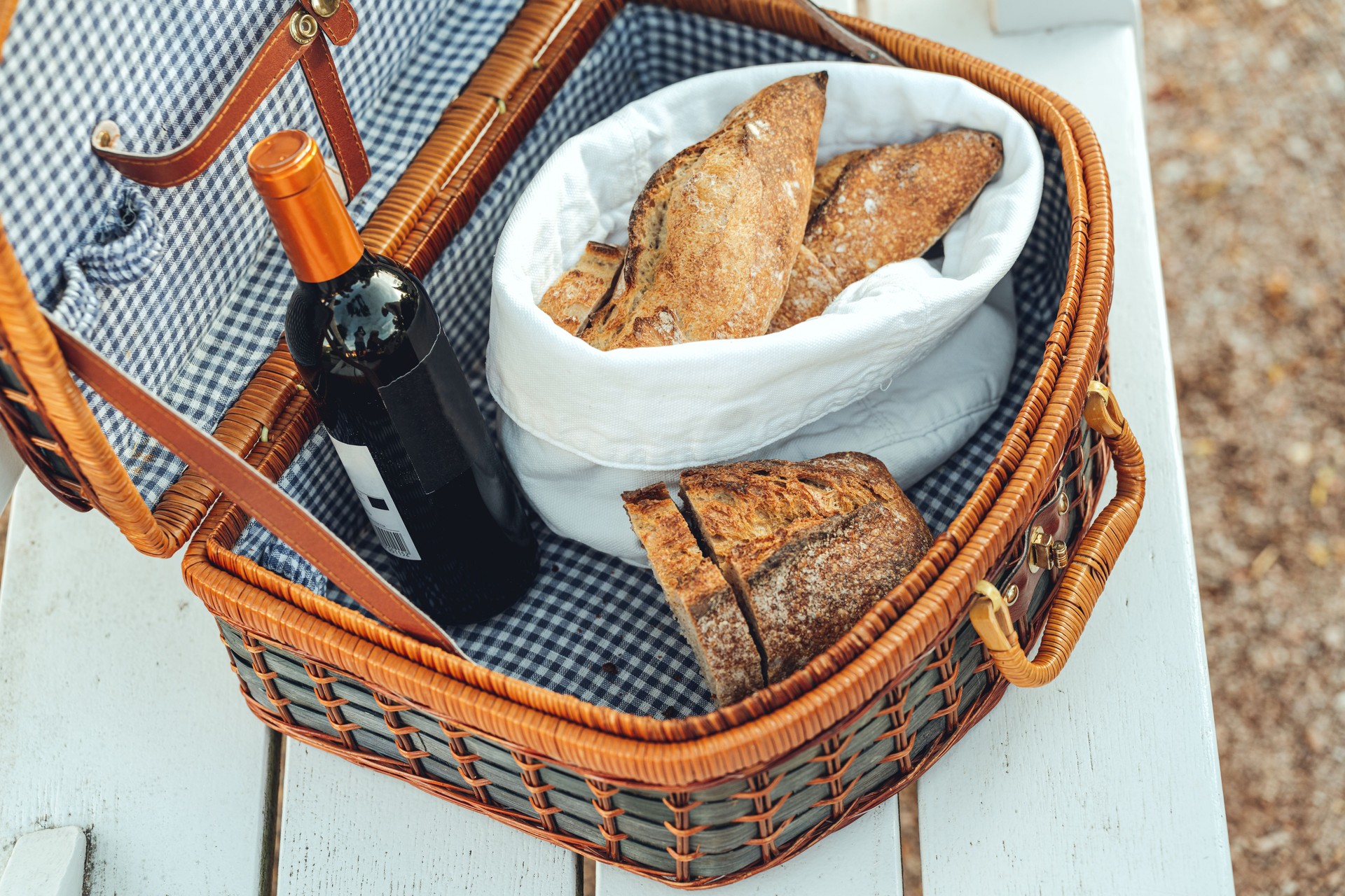Picnic basket with wine and bread on white bench