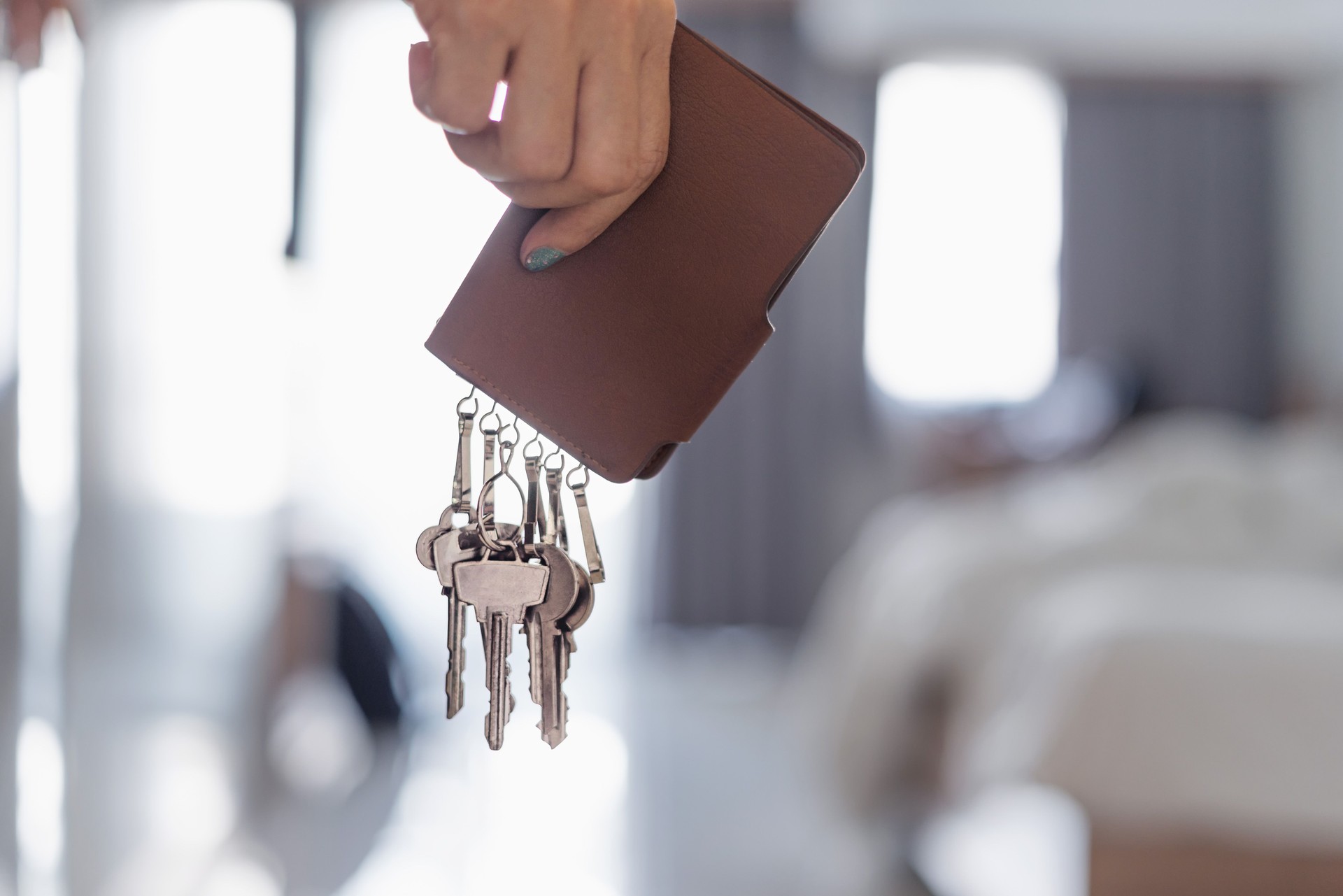 Female hand holding brown leather key holder in bedroom